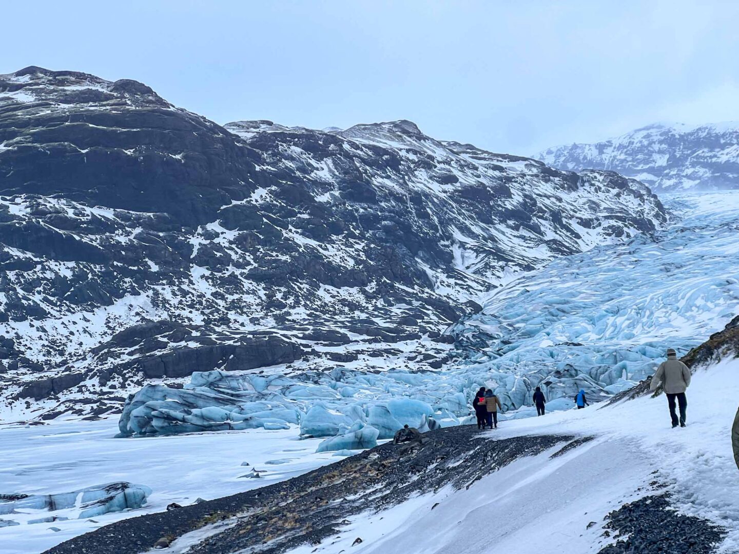 The Wandering Quinn Travel Blog what to wear in Iceland in winter, tourists walking towards glacier in winter in iceland