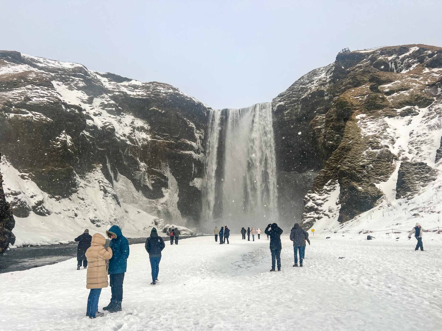 The Wandering Quinn Travel Blog what to wear in Iceland in winter, tourists at waterfall in iceland in winter clothes